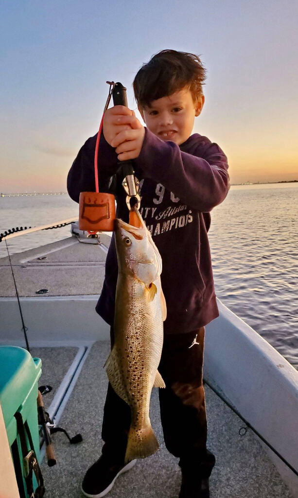 Child holding up fish on boat.