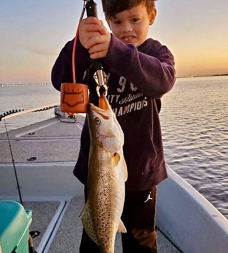 Child holding up fish on boat.